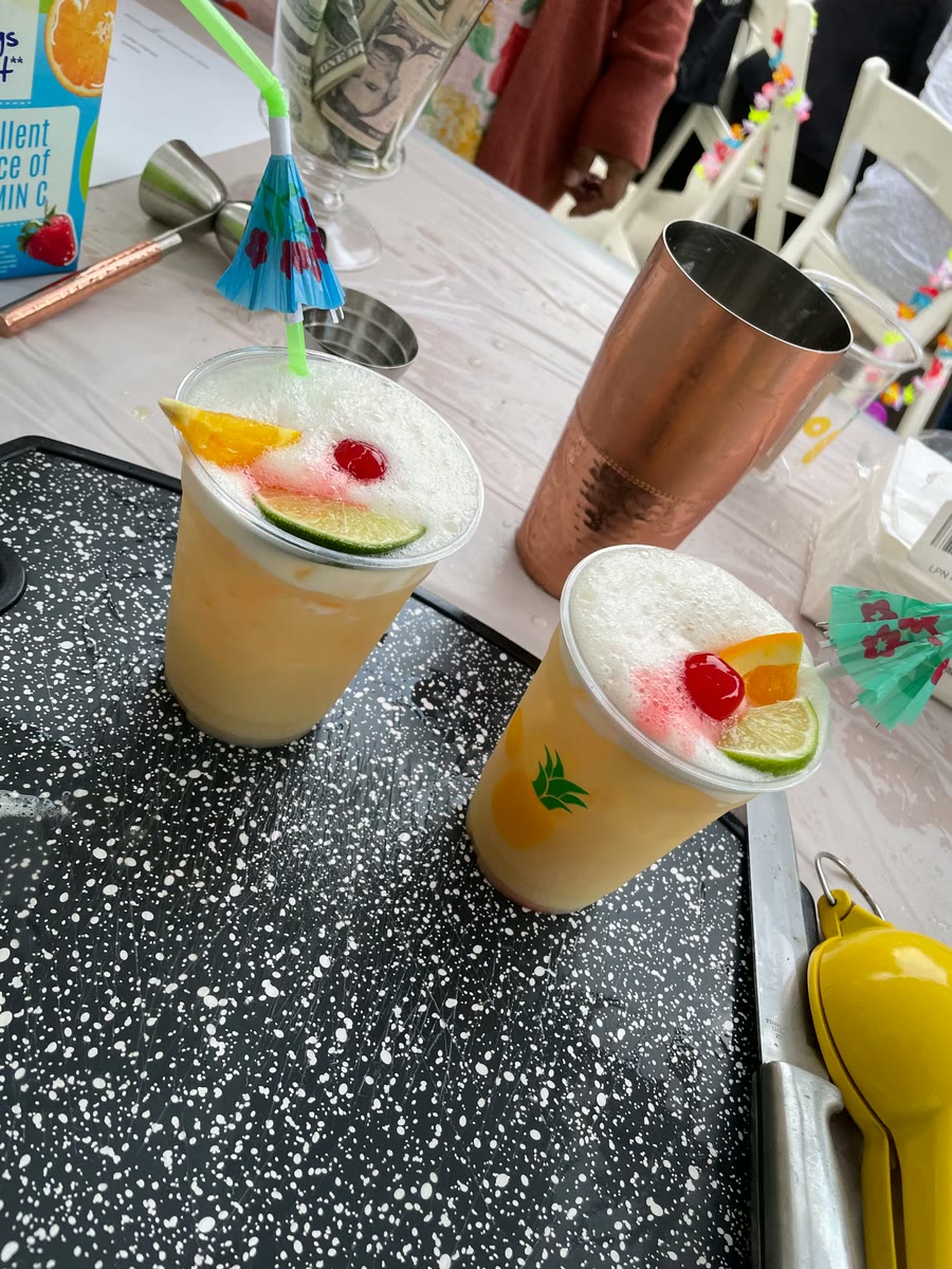 Two frothy tropical cocktails with cherries, citrus and paper umbrellas at a bar station