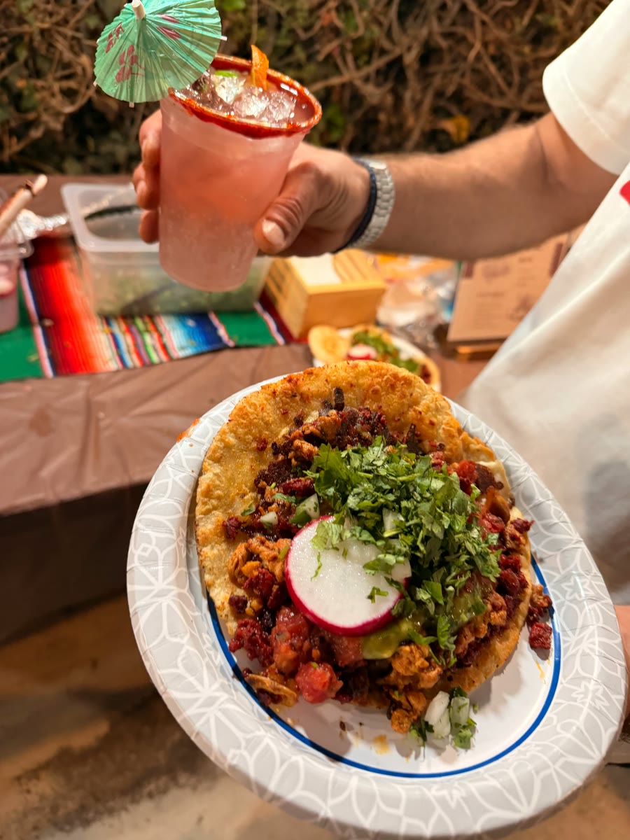 A taco loaded with meat, cilantro and radish beside a chili-rimmed pink cocktail